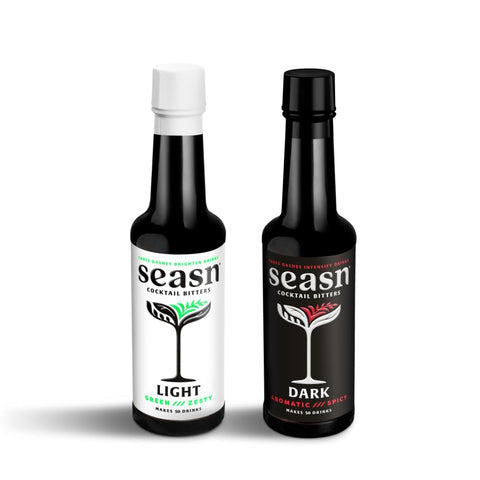 Two bottles of non-alcoholic cocktail bitters, one labeled 'LIGHT' with a green leaf design and one labeled 'DARK' with a red cocktail glass design, both with white and black elements on the labels.